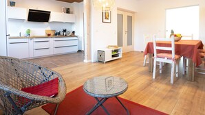 A modern kitchen with white cabinets, a dining area with a table and chairs, and a wicker chair with a red cushion. - Pure relaxation in the idyllic Heimig forest (Suhl Ot. Schmiedefeld am Rennsteig)