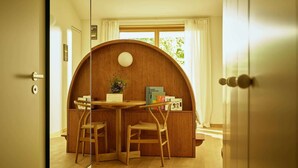 A cozy reading nook with a curved wooden wall, a round table, two chairs, and a small bookshelf with books. - Auberge Port Gitana (Bellevue)