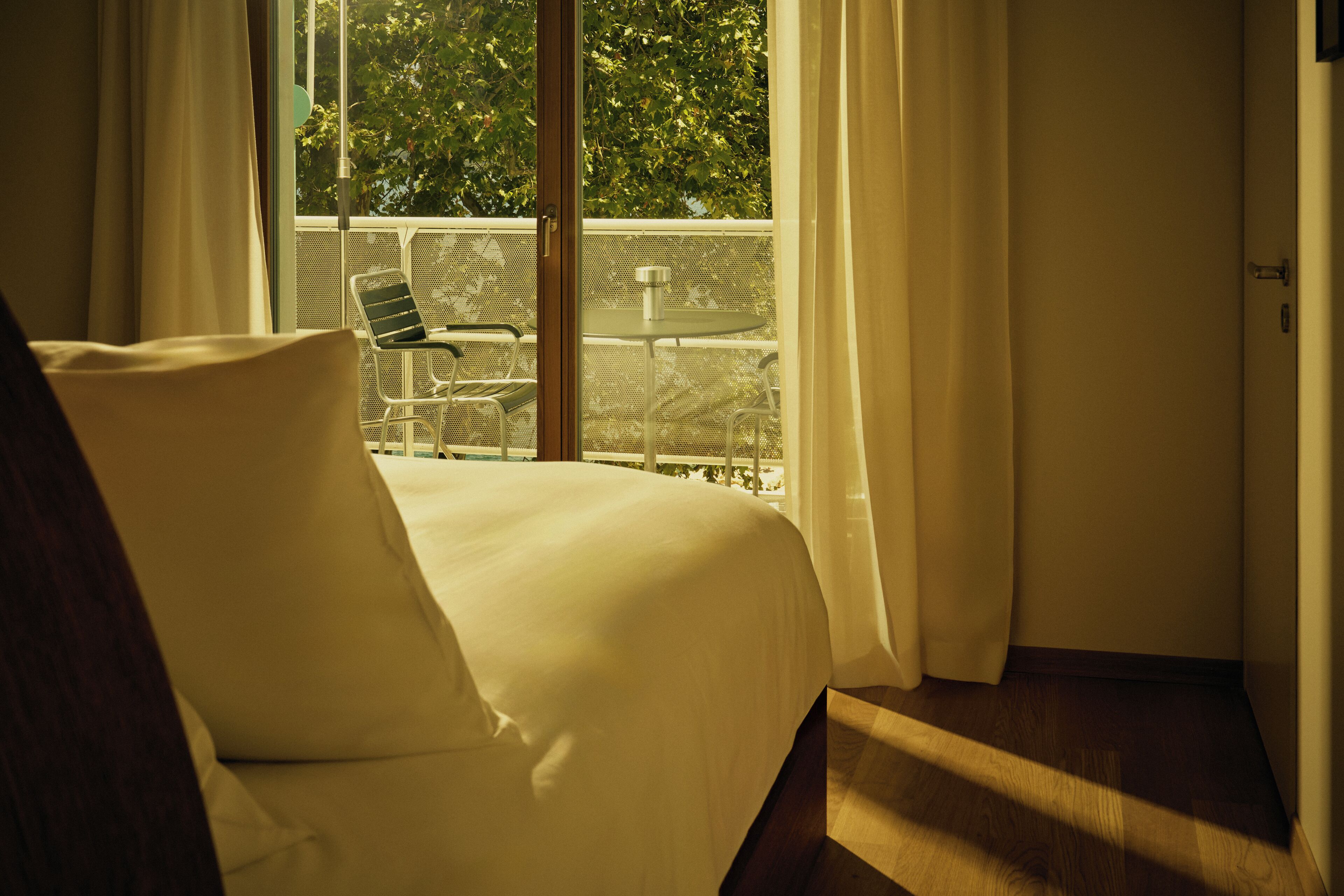 A hotel room with a bed, a chair, and a table near a window with a view of trees.