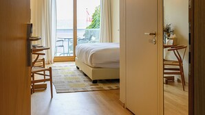 A hotel room with a bed, a desk, a chair, and a sliding door leading to a balcony with a table and chairs. - Auberge Port Gitana (Bellevue)