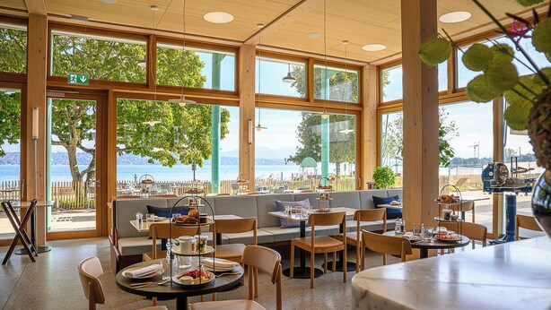 A restaurant with large windows offering a view of the sea. There are tables and chairs arranged for dining. - Auberge Port Gitana (Bellevue)