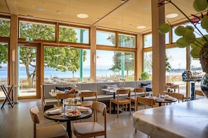 A restaurant with large windows offering a view of the sea. There are tables and chairs arranged for dining. - Auberge Port Gitana (Bellevue)