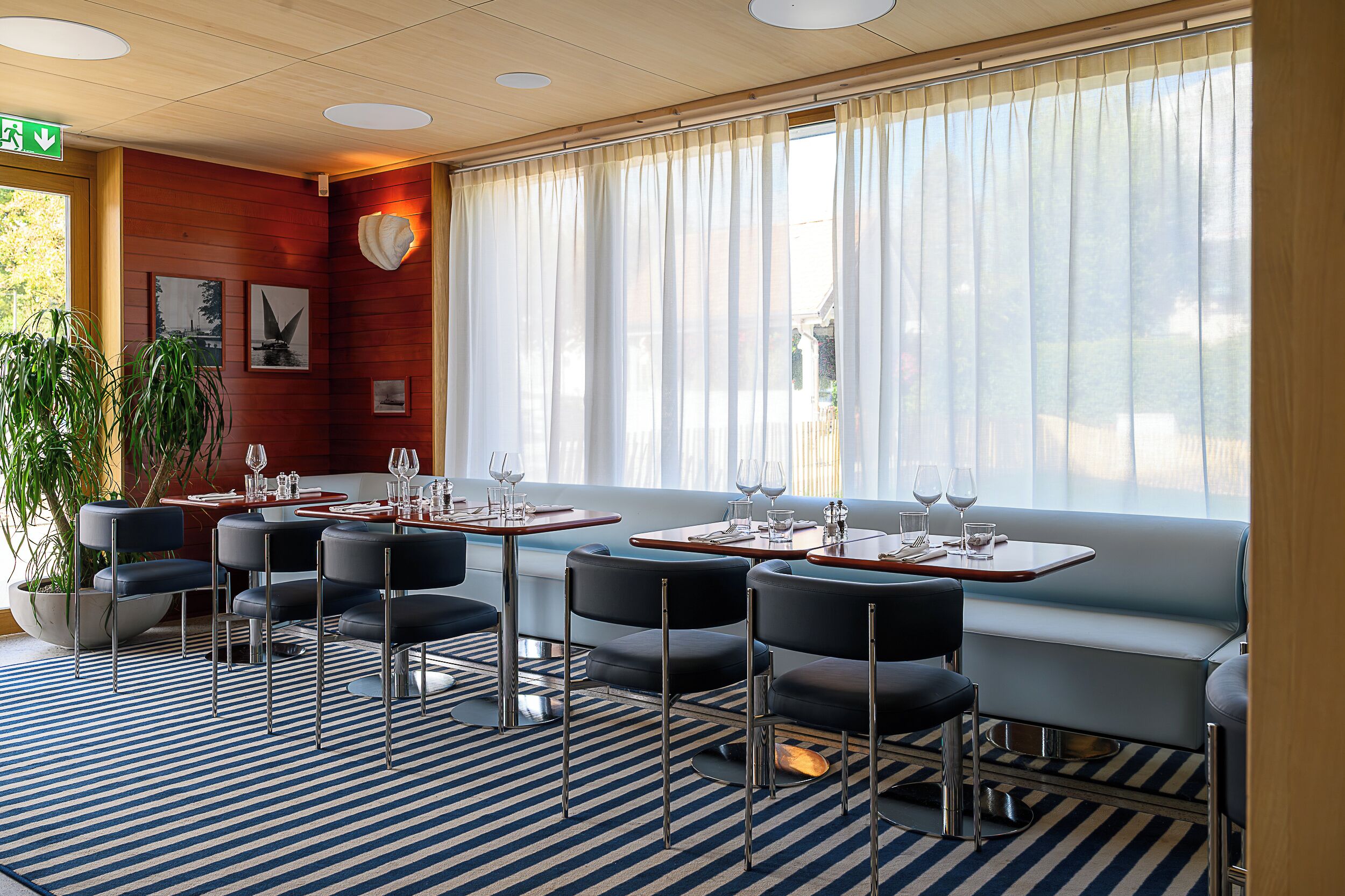 Ein Restaurant mit blau gestreiftem Teppich, schwarzen Stühlen und Tischen, die mit Weingläsern gedeckt sind.