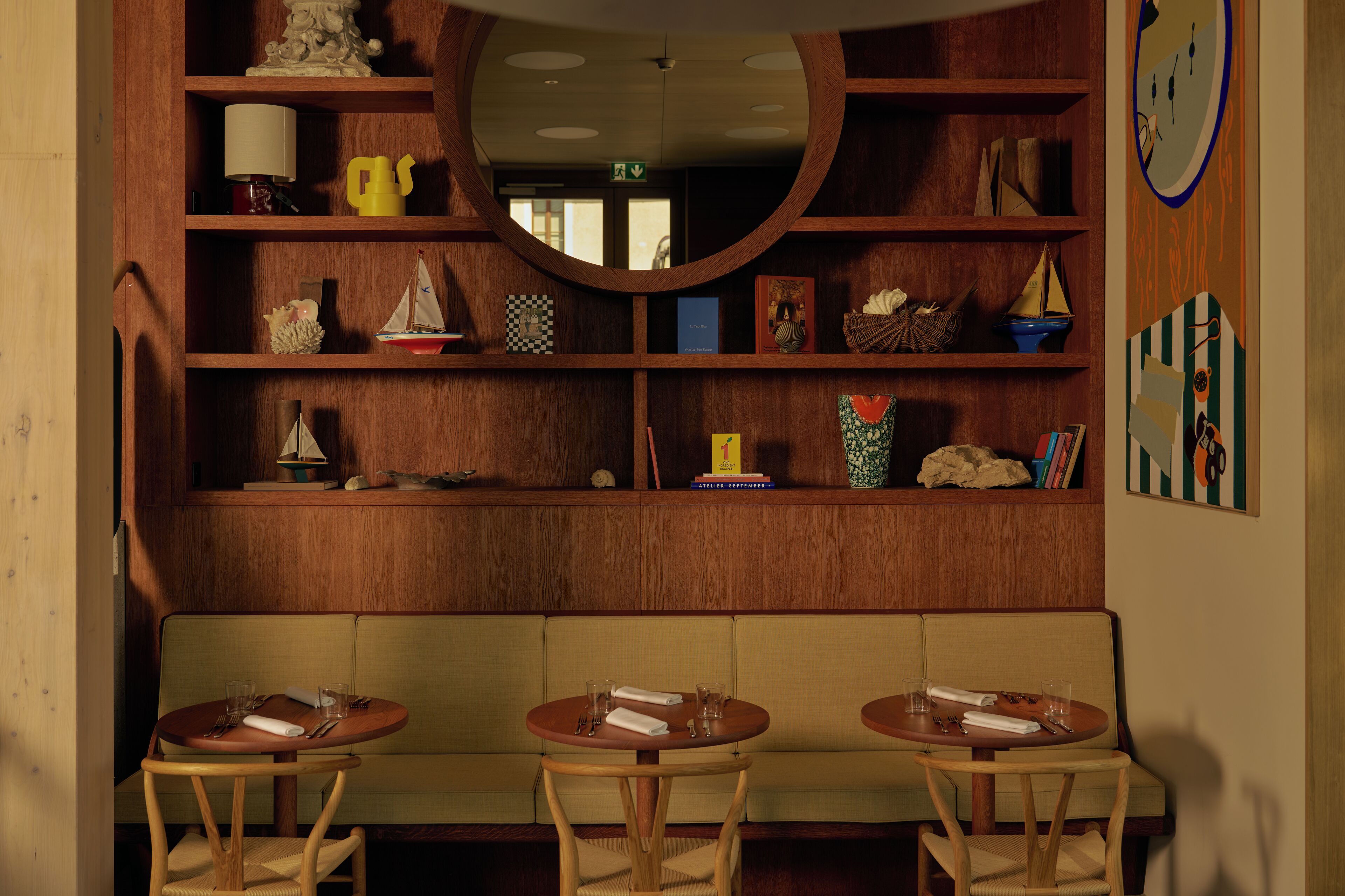 A cozy room with a wooden bookshelf, a round mirror, and a seating area with two round tables and chairs.
