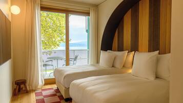 A hotel room with two beds, a wooden accent wall, a view of the outdoors, and a small table and chairs by the window.