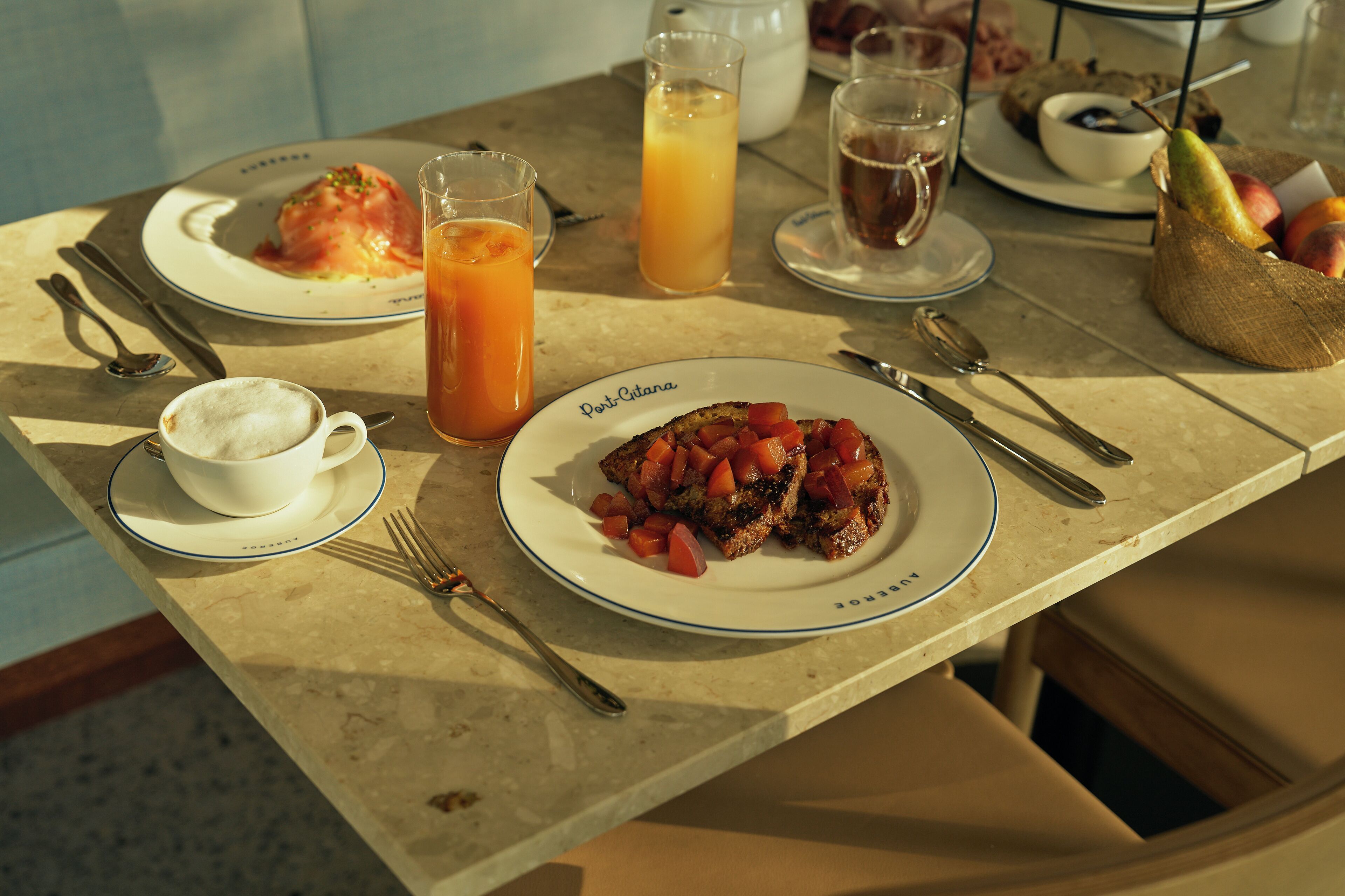 A breakfast table with plates of food, a coffee cup, and a fruit basket.