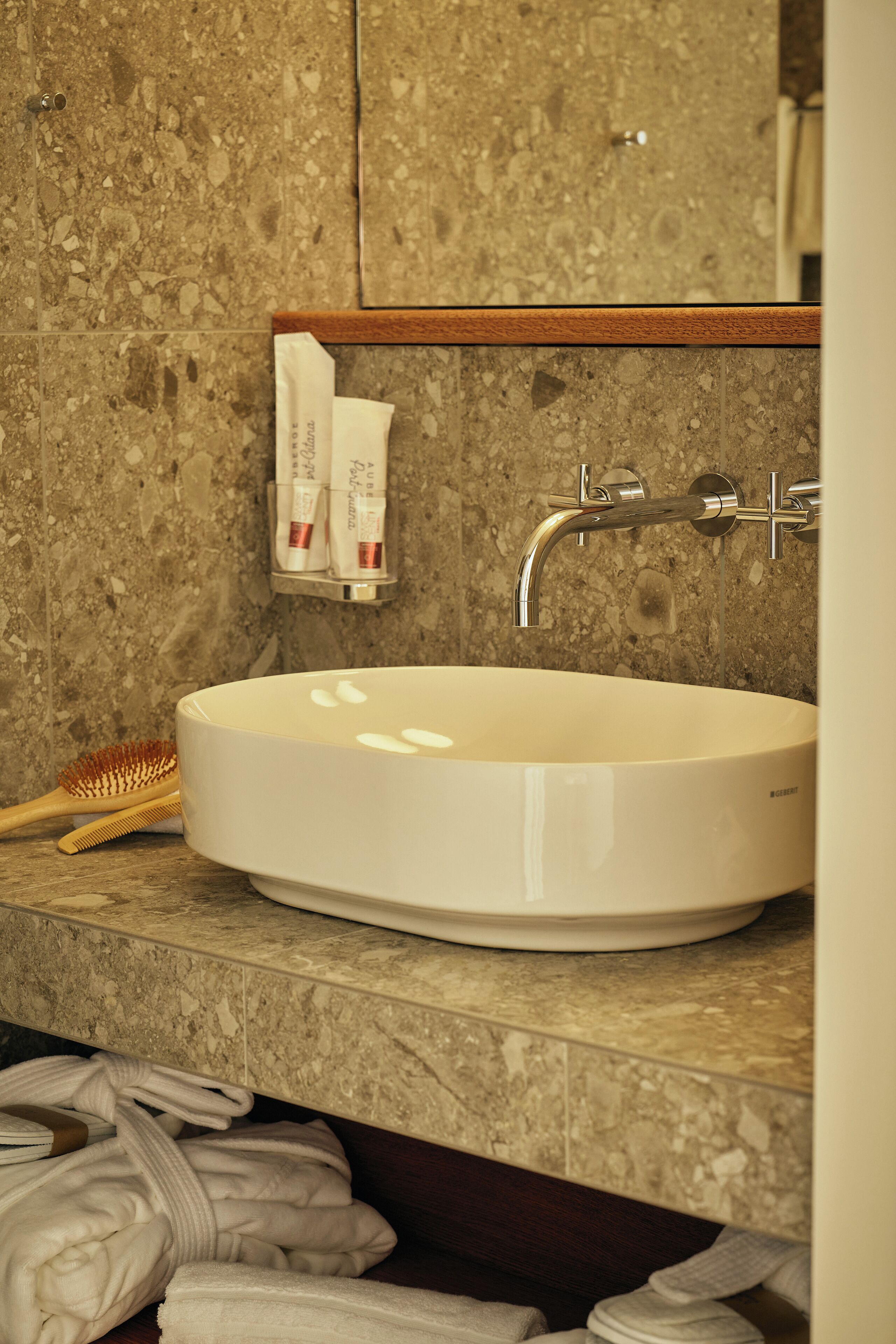 A bathroom with a white sink, a wooden-framed mirror, and toiletries on a shelf.
