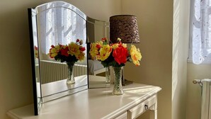 Uma toucador com espelho, dois vasos com flores e uma lâmpada.