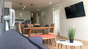 En moderne stue med sofa, spisebord, stole, fjernsyn og ventilator.