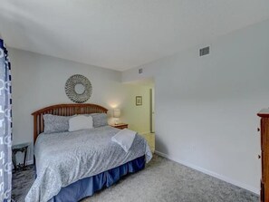 A bedroom with a bed, bedside table, lamp, and a decorative wall piece.