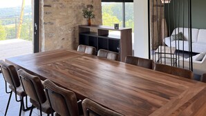 A spacious dining area with a long wooden table and chairs, a staircase with a wooden railing, and a view of the outdoors. - "La Grange de La Contie" (Perpezac-le-Blanc)