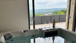 A hot tub with a view of the countryside through a large window. - "La Grange de La Contie" (Perpezac-le-Blanc)