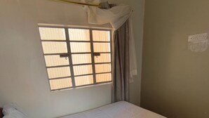 A small, single-bed room with a window, a curtain, and a wall-mounted light fixture. - Charming bed & breakfast with WiFi in Nyeri (Nyeri)
