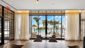 A modern dining area with a large table and chairs, large windows with curtains, and a view of palm trees and a pool.