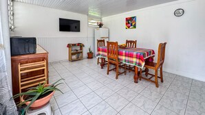 A dining area with a table covered by a colorful tablecloth, surrounded by wooden chairs. A television is mounted on the wall, and a potted plant is on a stool. - Mont loué - Maison 6 personnes (Trois Rivieres)