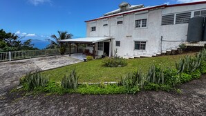 A two-story building with a red roof, a covered porch, and a small garden with tropical plants. - Mont loué - Maison 6 personnes (Trois Rivieres)