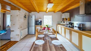A modern kitchen with wooden beams, a dining table set for six, and a large window.