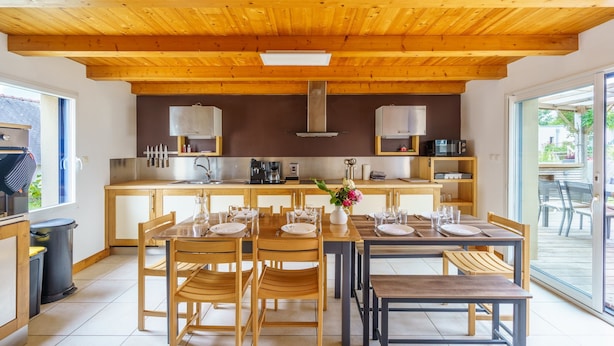 A modern kitchen with wooden beams, a central island, and a dining area with wooden chairs and tables.