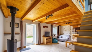 A spacious living room with a high ceiling, wooden beams, a fireplace, a television, and a sofa.