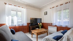 Una sala de estar con un sofá, una mesa de centro, un televisor y una ventana con cortinas.