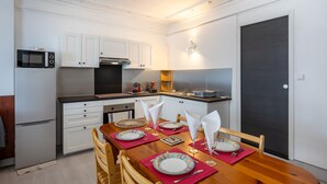 Una cocina compacta con muebles blancos, microondas y estufa. Hay una mesa de comedor con platos, vasos y cubiertos.