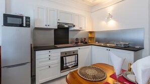 Una cocina moderna con armarios blancos, horno empotrado, microondas y una mesa de comedor de madera con un mantel individual.