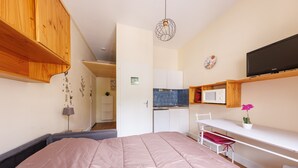Ein Schlafzimmer mit Bett, Schreibtisch, Fernseher und einer Küchenzeile.