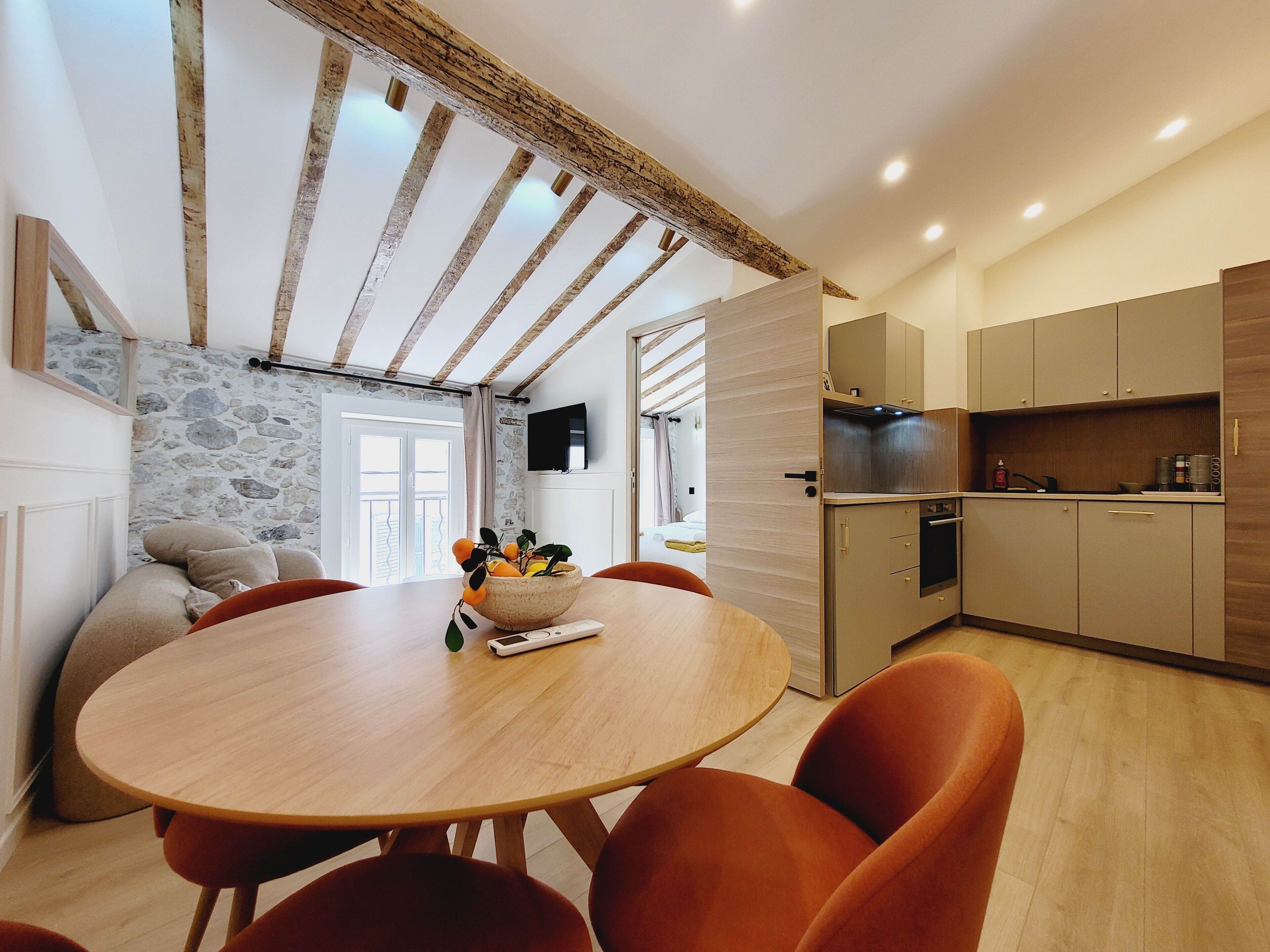 Een moderne keuken met houten kasten, een inbouwoven en een eethoek met een ronde tafel en oranje stoelen.