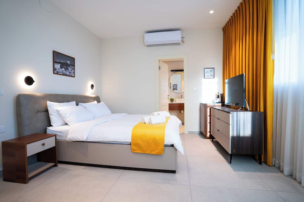 A modern hotel room with a bed, bedside table, TV, and a bathroom visible through an open door.