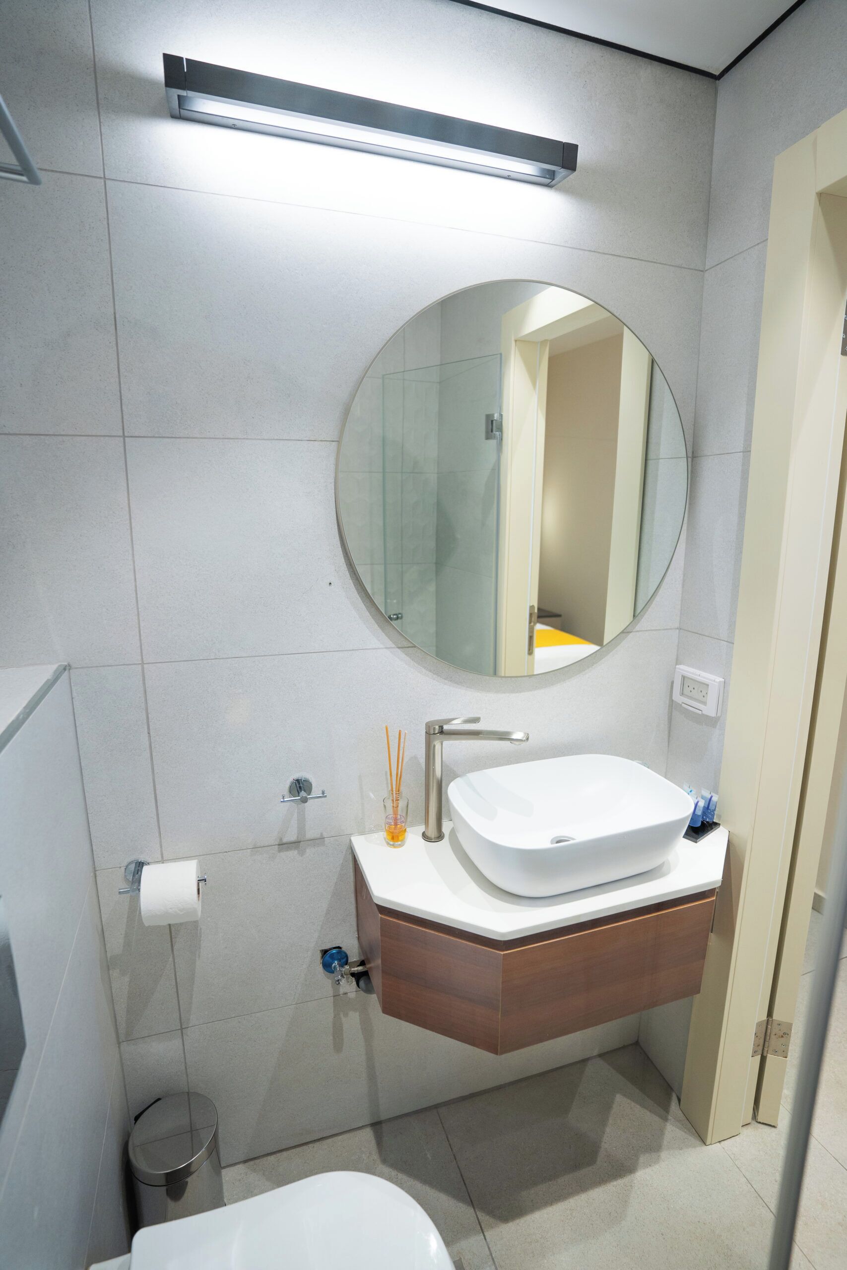 Een moderne badkamer met een wit wastafel, een ronde spiegel en een toilet.