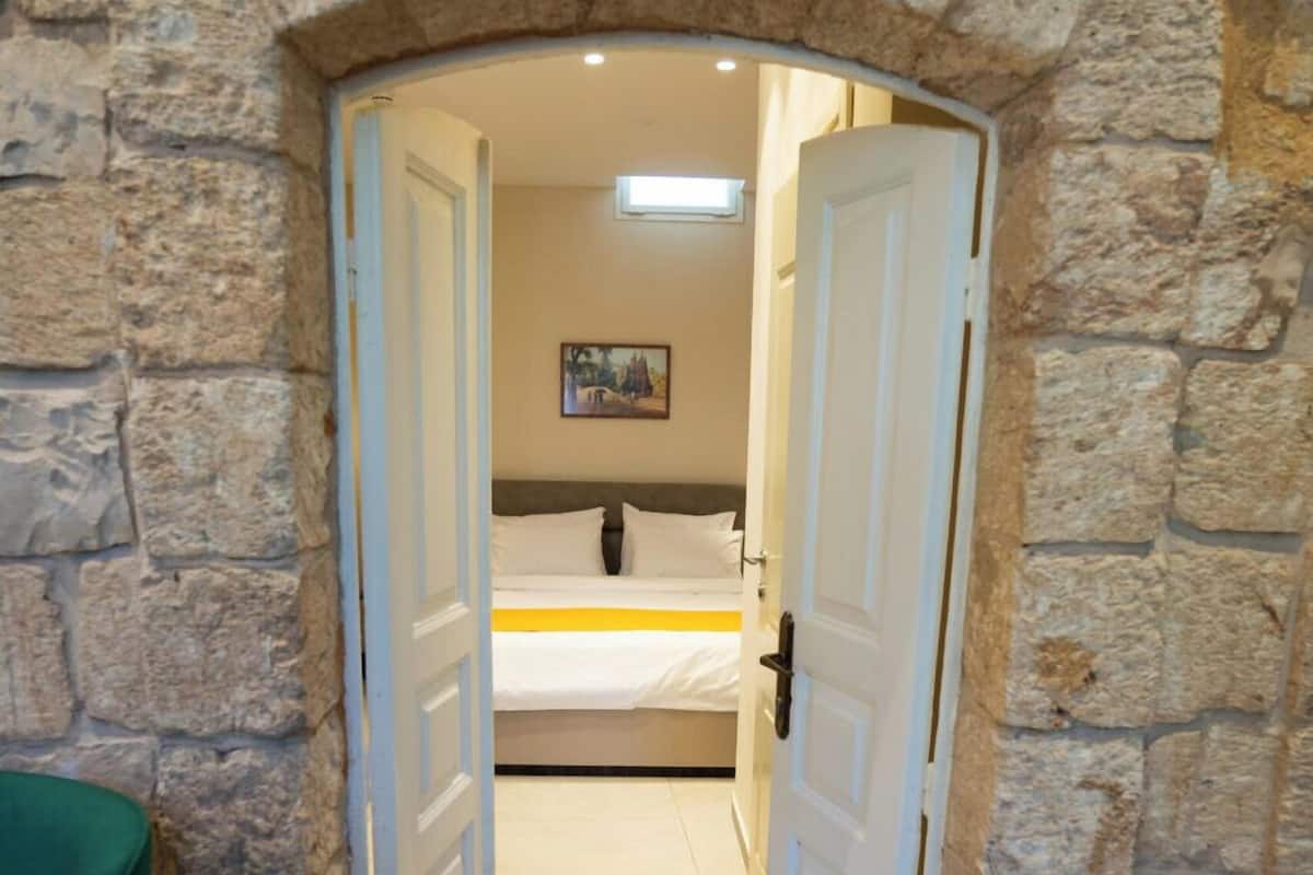 A stone-walled room with a bed, a door, and a green chair.