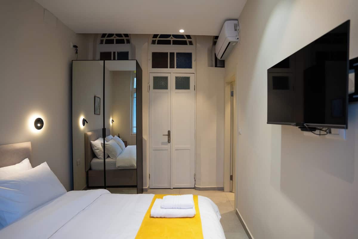 A hotel room with a bed, a wardrobe, a mirror, a TV, and an air conditioning unit.