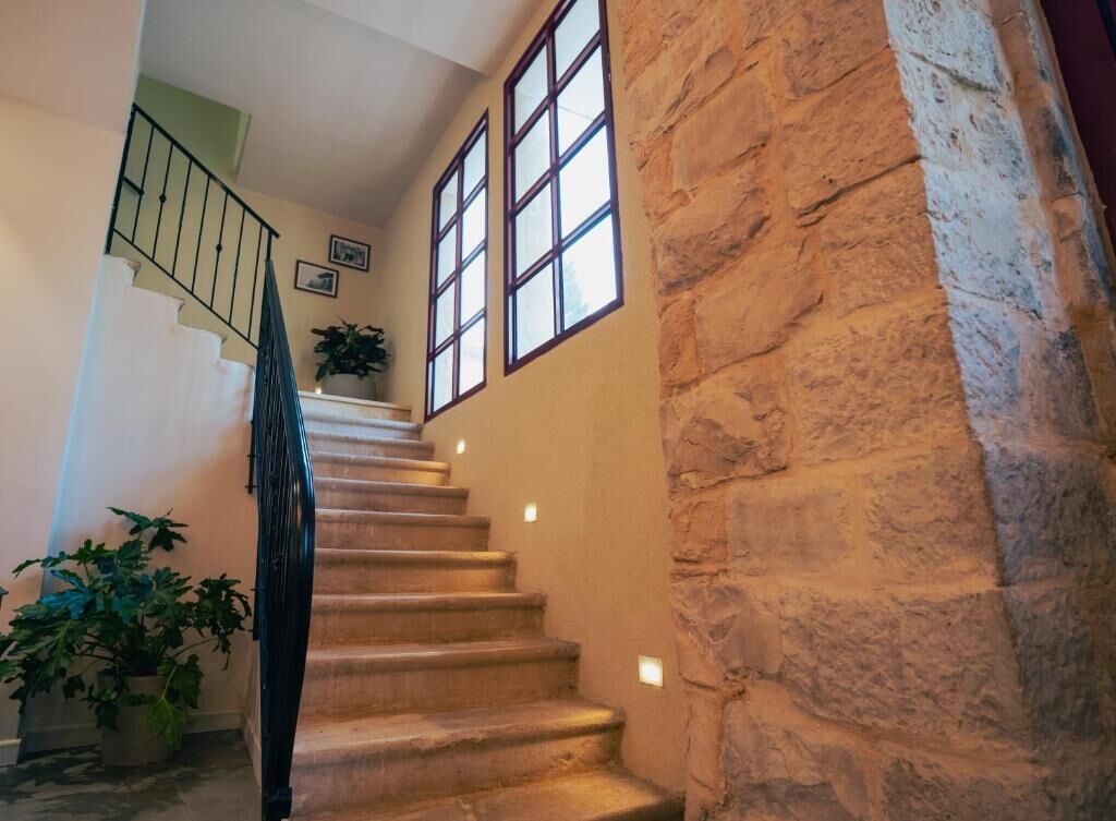 Un escalier en pierre avec une rampe en métal, des plantes en pot et une vue sur l’étage supérieur à travers de grandes fenêtres.