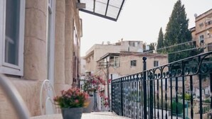 A balcony with a table and chairs, a potted plant, and a view of the surrounding buildings. - Roots Boutique Hotel (Nazareth)