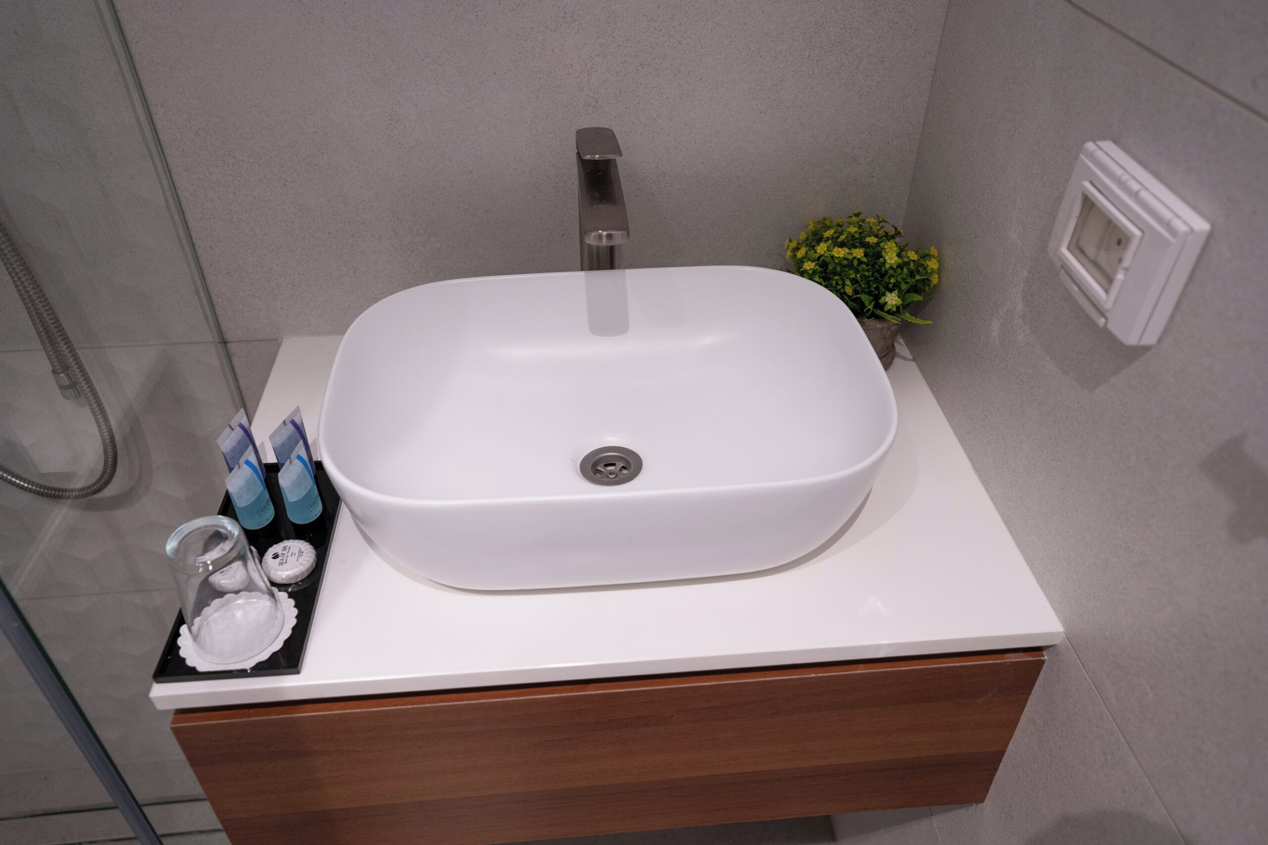 Un baño con lavamanos blanco, tocador de madera y una pequeña planta en maceta.