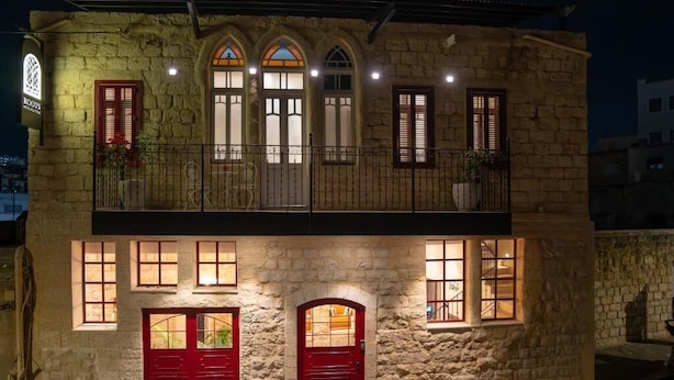 A two-story stone building with a balcony, red doors, and multiple windows. - Roots Boutique Hotel (Nazareth)