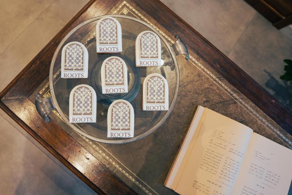 A glass tray with eight booklets labeled "ROOTS" on a wooden table next to an open book.