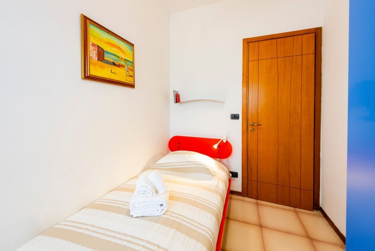 Una cama individual con una colcha a rayas, un cabecero rojo, una puerta de madera y un cuadro en la pared.