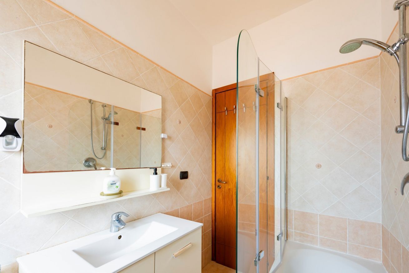 A bathroom with a glass shower enclosure, a white sink, a wooden door, and a large mirror.