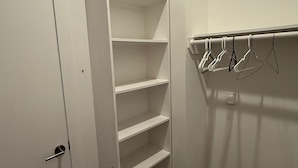 Een inloopkast met witte planken en een kledingroede.