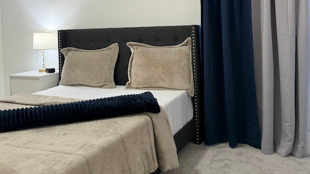 Een hotelkamer met een bed, nachtkastje, lamp en een raam met gordijnen.