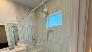 Een moderne badkamer met een douche met glazen wand, witte marmeren wanden en een grote spiegel.