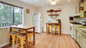 Una cocina con una mesa de madera, taburetes amarillos, un refrigerador, un microondas, una estufa y una ventana con vistas a árboles.