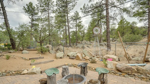 Un patio con una chimenea rodeada de taburetes de madera, con un fondo de pinos y un paisaje rocoso.