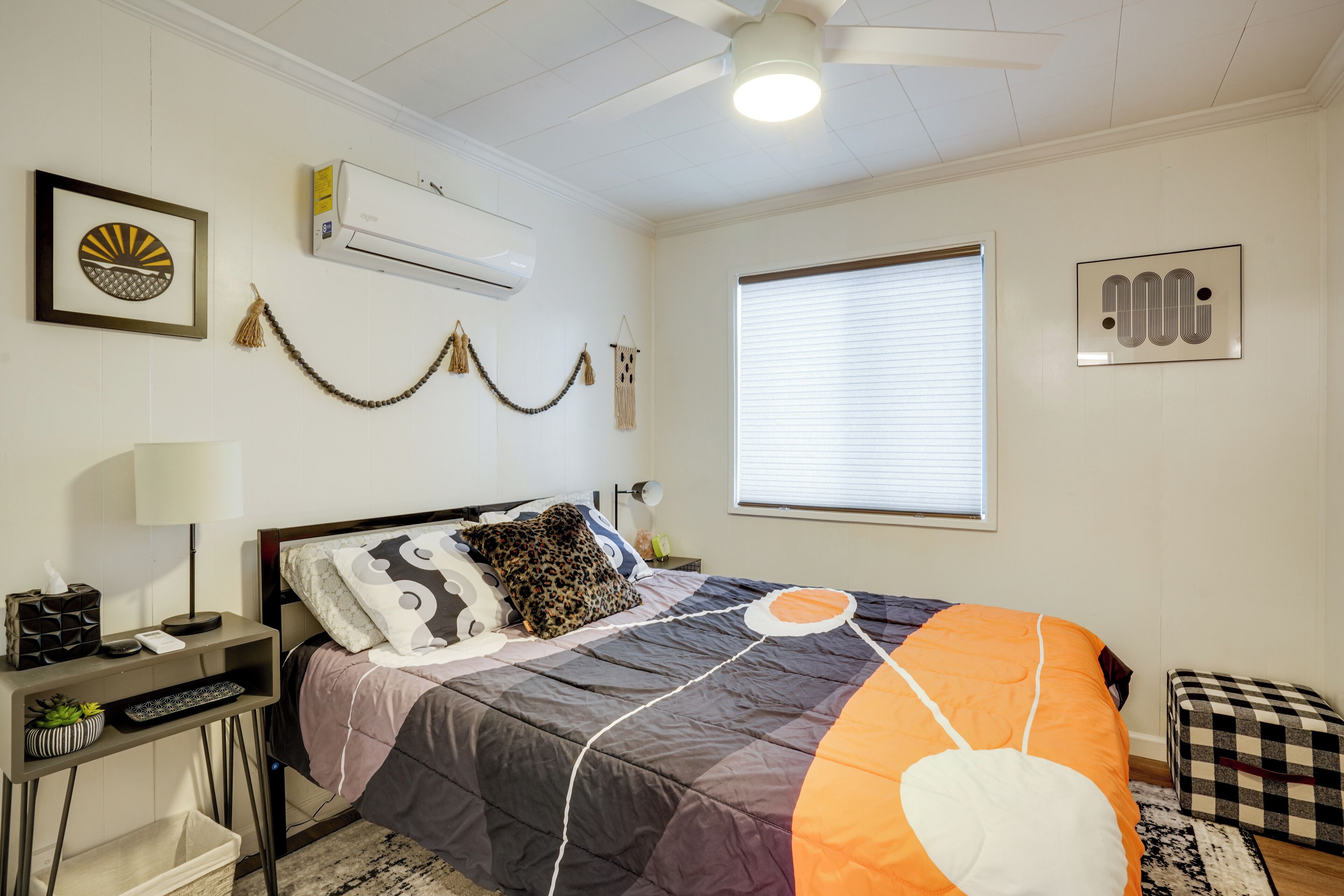 Un dormitorio con cama, mesita de noche, lámpara, unidad de aire acondicionado y una ventana con persianas.