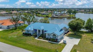 A large house with a blue roof, surrounded by a lake and other houses. - Poolside Bliss & Lake Fun: Florida Getaway! (Fort Ogden)