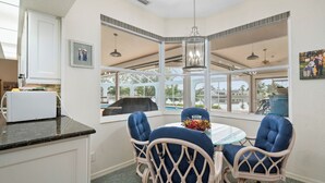 A corner dining area with a glass table, four blue upholstered chairs, a white wicker chair, and a hanging pendant light. - Poolside Bliss & Lake Fun: Florida Getaway! (Fort Ogden)