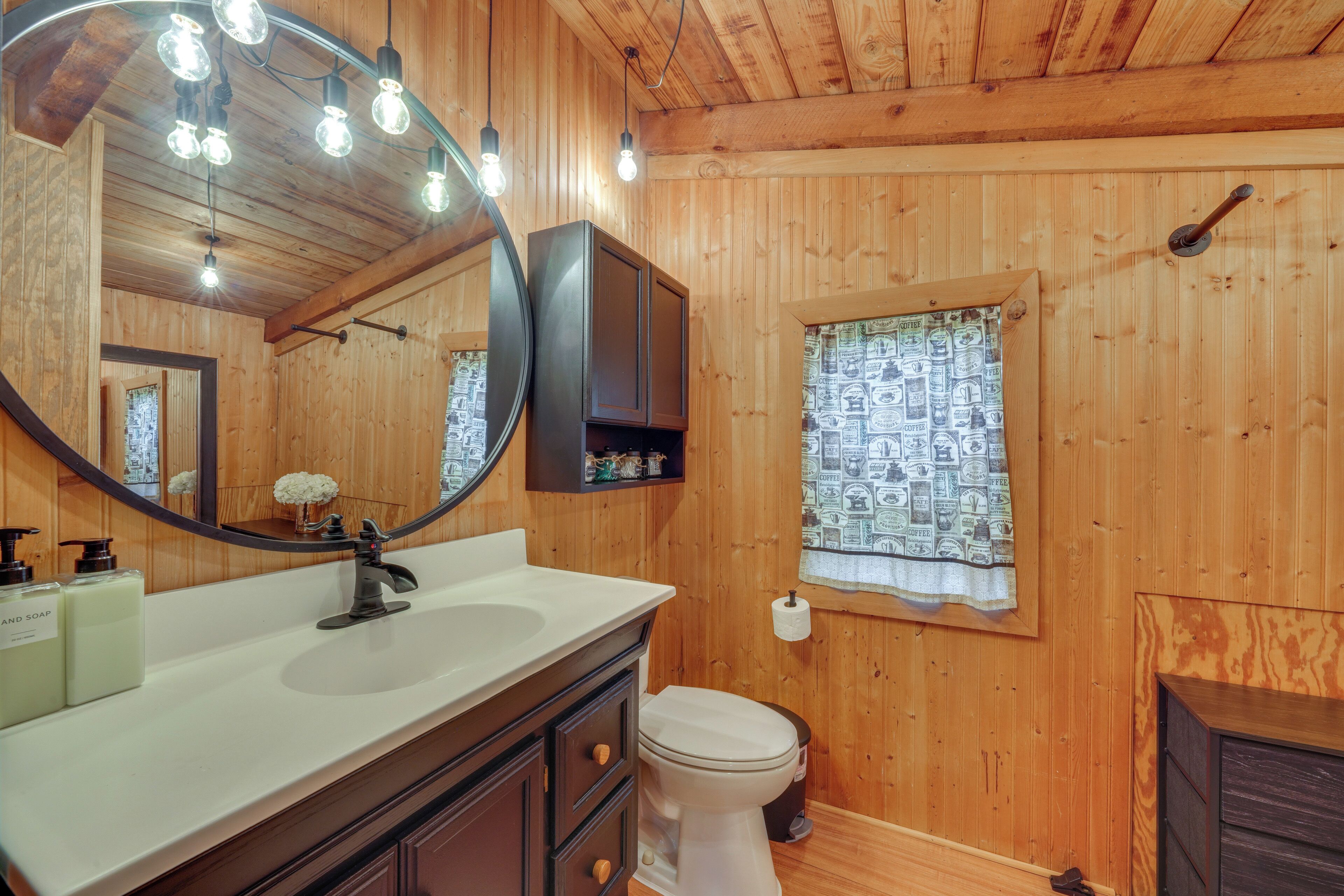 A bathroom with wooden walls, a large mirror, a sink with soap dispensers, and a toilet.
