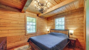 A wooden cabin bedroom with a bed, nightstands, and a chandelier. - < 1 Mi to Casinos: Countryside Louisiana Getaway! (Duson)