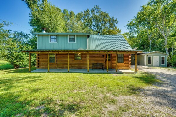 A log cabin with a covered porch and a small attached garage, surrounded by a grassy yard and trees. - < 1 Mi to Casinos: Countryside Louisiana Getaway! (Duson)